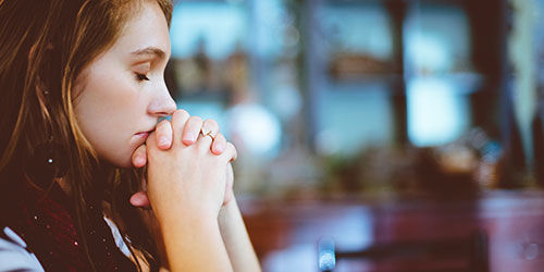 A young woman with her hands folded in prayer and eyes closed