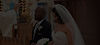 A bride and groom in their clothing receving a blessing from a priest