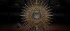 A gold monstrance with blue detail against a dark background