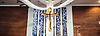 A Black Jesus against a wooden cross against a stained glass window and red brick wall
