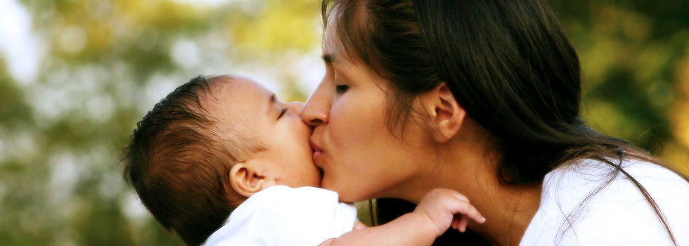 A woman with olive skin and dark hair kissing her baby on the cheek
