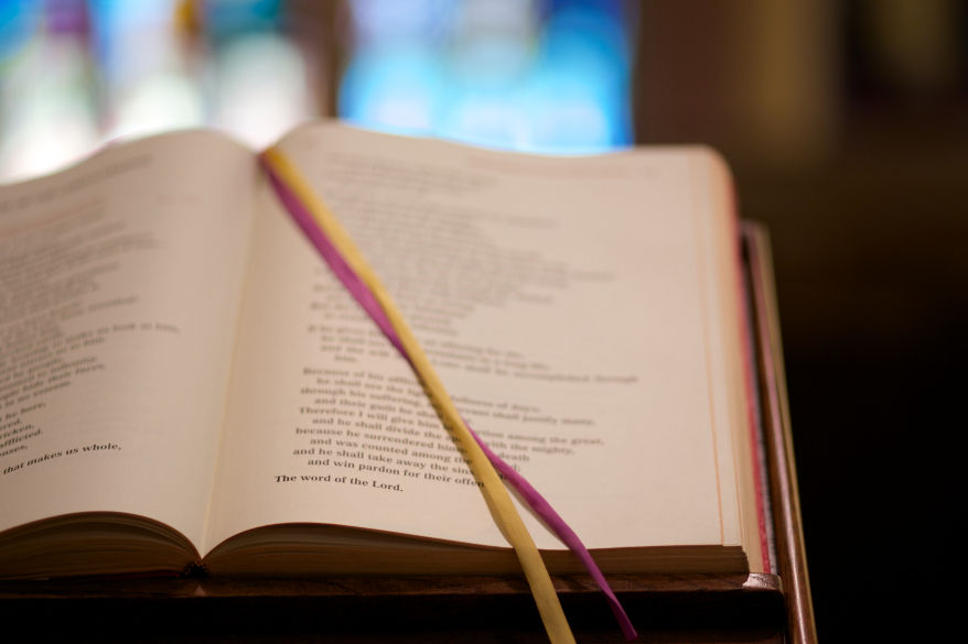 A book of readings with yellow and purple ribbons laying across an open page